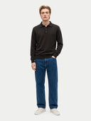 A man modeling a dark brown long-sleeve polo sweater paired with blue jeans and white sneakers, standing against a light gray studio background.