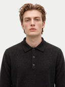 A man wearing a dark charcoal gray knit polo shirt, photographed from the chest up against a clean light gray background.