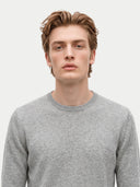 close up front view of a man wearing a man wearing a light gray crew neckline sweater on a light gray background.