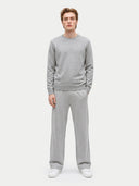 A man modeling a light gray crewneck sweatshirt and matching light gray sweatpants, paired with white sneakers, against a solid light gray background.