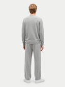 back view of a man standing wearing a light gray outfit, sweater, jogger pants and white sneakers on a light gray background.