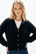 A blonde woman wearing a black button-up cardigan over a white t-shirt and blue jeans, photographed against a clean white studio background.