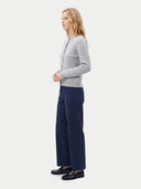 A woman stands in profile wearing a light gray cable-knit cardigan, navy blue wide-leg trousers, and black loafers against a plain light gray studio background.