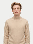 A man wearing a light beige knit mock neck sweater, photographed against a solid light gray background.