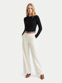 A woman modeling a black ribbed long-sleeve top and off-white wide-leg trousers with a thin brown belt, standing against a light gray studio background.
