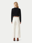 A woman shown from the back wearing a black ribbed long-sleeve top, off-white wide-leg trousers, a brown belt, and brown ankle boots, against a light gray studio background.