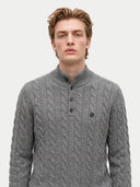 close up front view of a man standing wearing a gray cable knit, half buttoned cardigan with mock neckline.