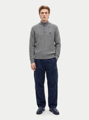 A male model wearing a gray cable-knit mock-neck sweater with a button placket, paired with navy blue cargo pants and dark loafers, standing against a light gray studio background.