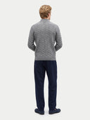 back view of a man standing wearing a gray cable knit cardigan and navy pants with navy flats on a light gray background.