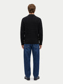 A man viewed from behind wearing a black cable-knit sweater and blue jeans against a light gray studio background.