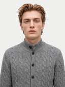 A man wearing a gray cable-knit button-up sweater with a stand collar, photographed against a plain light gray background.