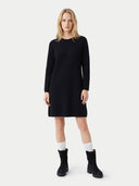 A blonde woman modeling a black long-sleeve knit dress with a crew neck, paired with white socks and black ankle boots, against a light gray studio background.