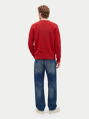 A man viewed from behind wearing a red crewneck sweatshirt, blue jeans, and white sneakers against a light gray studio background.