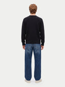 A man viewed from behind wearing a black long-sleeve crewneck sweater, blue jeans, and white sneakers against a light gray studio background.