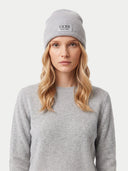 A woman wearing a light gray ribbed knit beanie with a black GOBI EST. 1981 logo patch on the front, paired with a matching light gray crewneck sweater, against a plain light gray background.