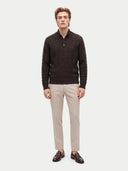 A man modeling a dark brown cable-knit polo sweater, paired with beige trousers and brown leather loafers, against a light gray studio background.