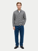 A man modeling a gray cable-knit button-up cardigan over a white t-shirt, paired with blue jeans and black leather shoes, against a light gray studio background.