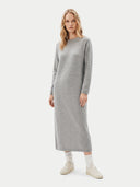 A woman modeling a light gray long-sleeve knit midi dress with a crew neck, paired with white socks and off-white sneakers, against a solid light gray background.