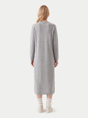 A woman viewed from the back wearing a light gray long-sleeve knit midi dress, cream socks, and off-white boots against a plain light gray studio background.