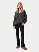 A woman modeling a dark gray heathered v-neck sweater, black pants, and brown suede shoes against a light gray studio background.