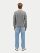 A man viewed from behind wearing a gray cable-knit sweater and light blue jeans against a light gray studio background.