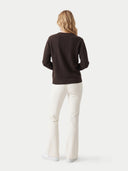 A woman shown from the back wearing a dark brown long-sleeve knit sweater and off-white flared pants against a light gray studio background.