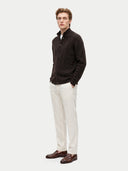 A man modeling a dark brown textured knit cardigan over a white collared shirt, paired with off-white trousers and brown leather loafers, against a light gray studio background.