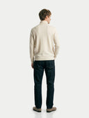 back view of a man wearing a beige turtle neck sweater and dark jeans standing against a white background #color_off-white