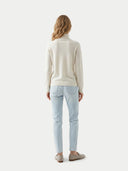 back view of a woman wearing a cream turtle neck sweater and light blue jeans on a white background  #color_white