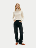 Woman wearing a cream turtleneck sweater and black jeans on a white background