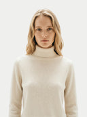 Woman wearing a beige turtleneck sweater against a white background