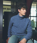 Man wearing a blue turtleneck sweater sitting indoors.