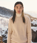 Person wearing a beige sweater in a snowy mountain landscape
