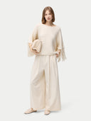 front view of a woman wearing a beige cashmere poncho with fringed sleeves, over a white outfit. #color_white