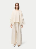 front view of a woman wearing a beige cashmere poncho with fringed sleeves, over a white outfit. #color_white