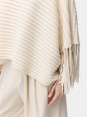 close up side view of a woman wearing a beige cashmere poncho with fringed sleeves, over a white outfit. #color_white