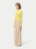 side view of a woman wearing a yellow cardigan with hidden buttons and beige pants on a light gray background. #color_blazzing-yellow