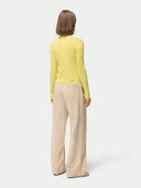 back view of a woman wearing a yellow cardigan with hidden buttons and beige pants on a light gray background. #color_blazzing-yellow
