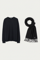 A black long-sleeve crewneck sweater displayed next to a matching black scarf with fringe, set against a solid off-white background. #color_black