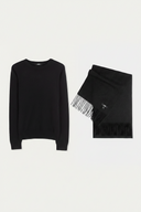 A black crewneck knit sweater and a matching black fringed scarf laid flat on a light gray background. #color_black