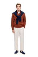Man in a coconut brown cashmere half-zip sweater with a dark indigo sweater tied over his shoulders, off-white trousers and navy loafers