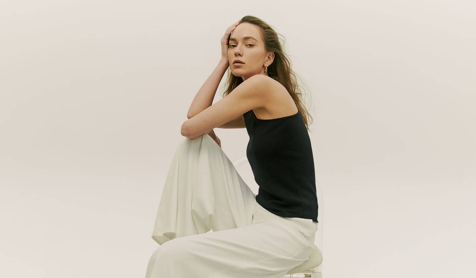Woman in black top and white pants sitting on a white background