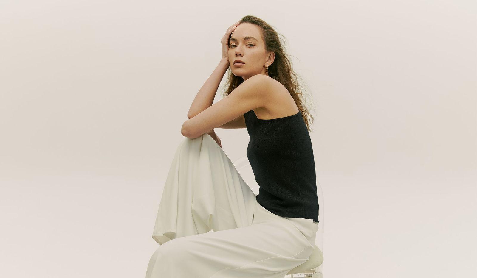 Woman in black top and white pants sitting on a white background