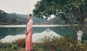 Woman in a pink dress standing by a lake with mountains in the background