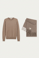 A taupe knit crewneck sweater displayed next to a matching fringed scarf with a small white embroidered letter T, set against a solid off-white background. #color_taupe