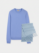 Flat lay of a light blue crew neck sweater and fringed scarf on a light gray background. #color_light-blue