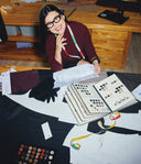Person in a sewing or design studio with fabric swatches and sewing tools.