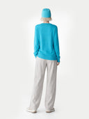 Person wearing a turquoise sweater and light gray pants on a white background #color_peacock-blue