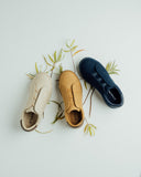 Three CashmereTech shoes in cream, tan and navy laid out with eucalyptus stems