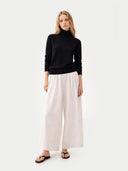 Woman wearing a black turtleneck sweater and white wide-leg pants on a white background #color_black